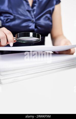 Un lavoratore dell'ufficio esamina i documenti attraverso una lente di ingrandimento Foto Stock