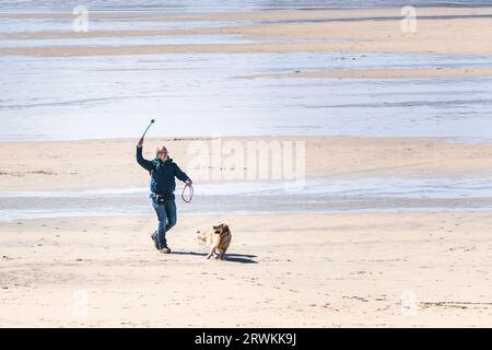 Un proprietario di cane che usa un lanciatore di palla per lanciare una palla per il suo cane da compagnia a Fistral Beach a Newquay in Cornovaglia in Inghilterra nel Regno Unito. Foto Stock