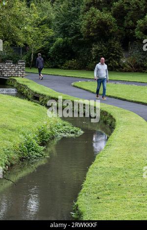 Persone che camminano lungo un sentiero vicino a un fiume che scorre attraverso i Trenance Gardens a Newquay, in Cornovaglia, nel Regno Unito Foto Stock