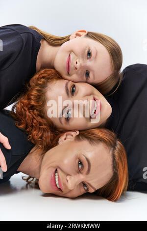 concetto di tre generazioni, donne felici e ragazze sorridenti che guardano la fotocamera sullo sfondo grigio Foto Stock