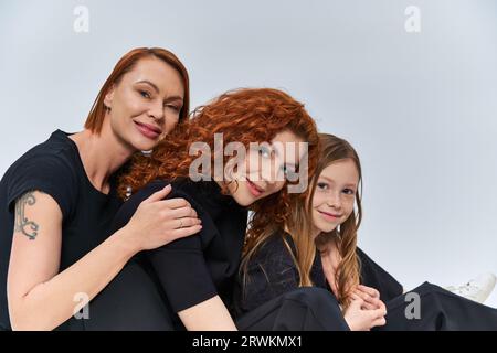 concetto di tre generazioni, allegra famiglia rossa sorridente e guardando la fotocamera su sfondo grigio Foto Stock