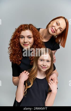 concetto di generazione femminile, famiglia felice con i capelli rossi in posa in abiti coordinati su sfondo grigio Foto Stock