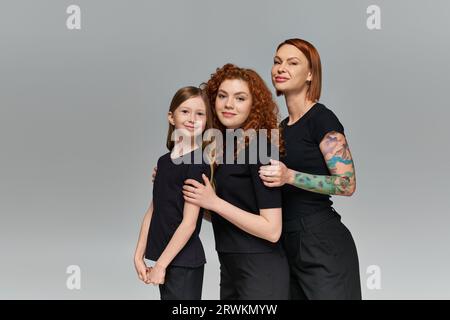 il concetto di generazione femminile, le donne con la testa rossa felice e i bambini in abbigliamento coordinato che si abbracciano su uno sfondo grigio Foto Stock