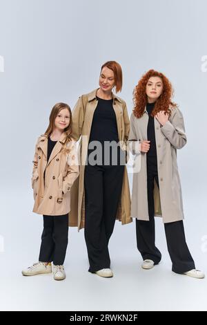 famiglia redhead in trench camici in posa insieme su sfondo grigio, tre generazioni di donne Foto Stock