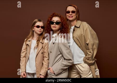 tre generazioni femminili, donne e bambini con capelli rossi che si mettono in posa con occhiali da sole e cappotti marroni Foto Stock
