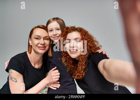 concetto di generazione femminile, donne rosse che scattano selfie con ragazza lentiggina su sfondo grigio Foto Stock