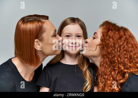 concetto di generazione femminile, donne rosse che baciano le guance di ragazza lentiggina su sfondo grigio Foto Stock