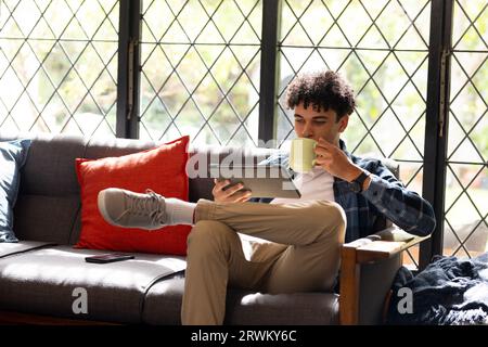 Felice uomo birazziale che lavora a casa usando tablet e bevendo Foto Stock