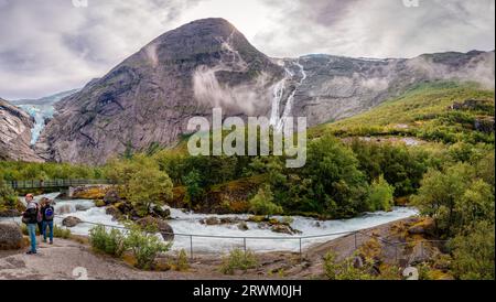 Briksdalen, Norvegia - 22 2022 agosto: Il fiume Briksdalselva con il ponte pedonale e il Briksdalsbreen (il ghiacciaio) sulla sinistra, nel Jostedalsbre Foto Stock