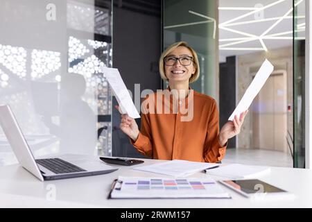 Finanziatrice donna d'affari felice e di successo felice del risultato ottenuto, celebrando la vittoria sul posto di lavoro all'interno dell'ufficio, lavoratrice che tiene in mano rapporti contrattuali e conti. Foto Stock