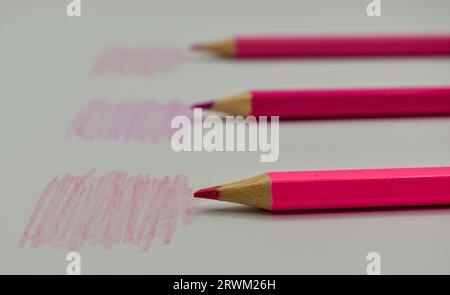 Tre matite rosa posizionate su una carta bianca accanto alle rispettive tonalità di colore. Foto Stock