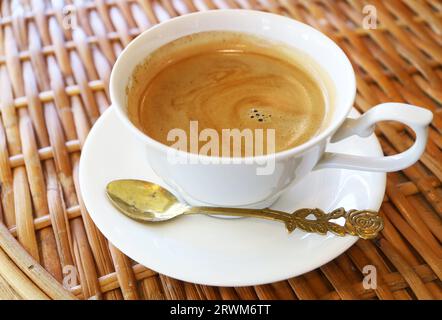 Tazza di caffè caldo con cucchiaio isolato su un tavolo in rattan Foto Stock