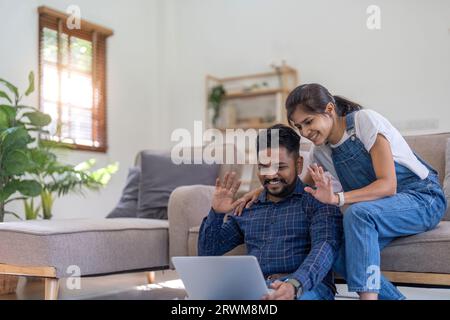 Coppia di amici indiani che saltano la mano mentre si usa un computer portatile per videochiamare con la famiglia da casa Foto Stock