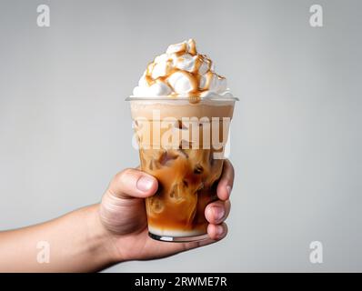 Immagine ravvicinata di una mano che regge un caffè freddo con panna montata e guarnizione al caramello Foto Stock