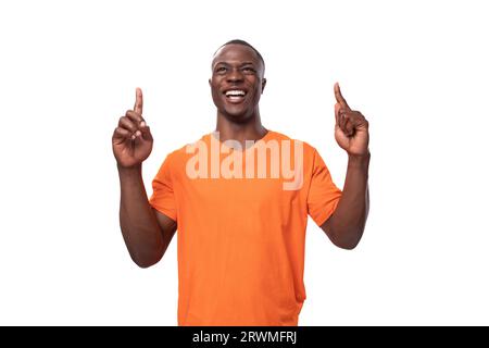 giovane americano vestito con una t-shirt arancione con stampa mockup che punta al dito alle notizie Foto Stock