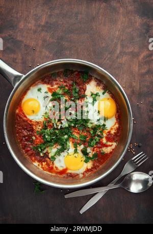 Shakshuka gustoso e salutare, omelette mediorientali in padella. Deliziose uova strapazzate cotte in salsa piccante di pomodoro e peperoni su una linguetta ruvida di legno Foto Stock