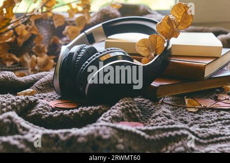 Audiolibro o podcast in autunno. Cuffie wireless con libri e foglie autunnali a maglia come concetto di apprendimento e istruzione, online co Foto Stock