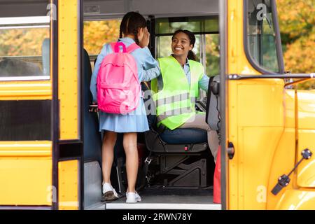 Trasporto. Little Girl dà High Five a driver Woman mentre entra a Schoolbus Foto Stock