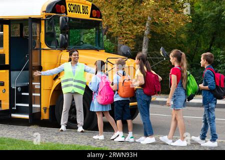 Insegnante donna nera che assiste i bambini mentre entrano in scuolabus Foto Stock