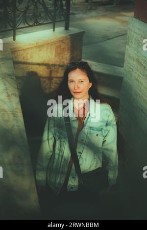 Una giovane donna con una giacca in denim in piedi su una scala. Motivi interessanti creati dalle ombre delle ringhiere giocano sul suo viso. I giovani An Foto Stock