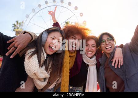Felice gruppo multietnico di amici che scattano una foto al parco divertimenti, guardando la fotocamera sorridente. Foto Stock