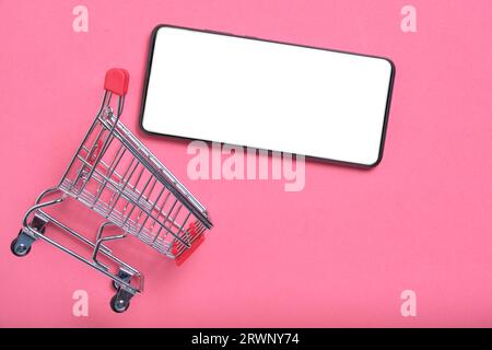 Carrello e cellulare con schermo bianco su sfondo rosa.Concept shopping online Foto Stock