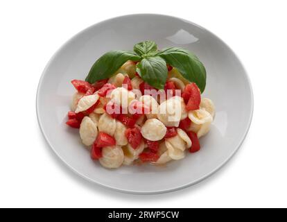 Orecchiette di pasta condita con pomodoro fresco, olio d'oliva e foglie di basilico in piatto bianco isolato su bianco con percorso di ritaglio incluso. Tipico Foto Stock