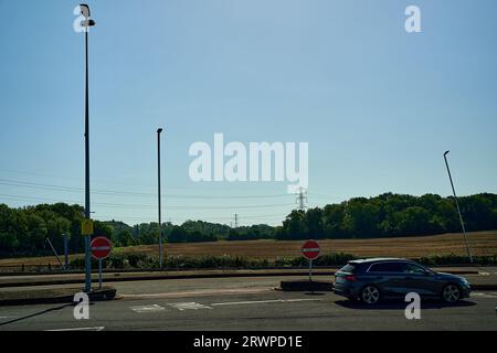 Inghilterra Regno Unito - 9 settembre 2023: Auto singola su parcheggio asfaltato con due segnali di ingresso sotto il cielo blu in estate e tre lampioni Foto Stock