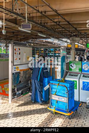 tokyo, giappone - 04 aprile 2023: Dipendente da dietro sulla piattaforma di una stazione ferroviaria giapponese che prende bottiglie e lattine da contenitori di plastica posti su Foto Stock