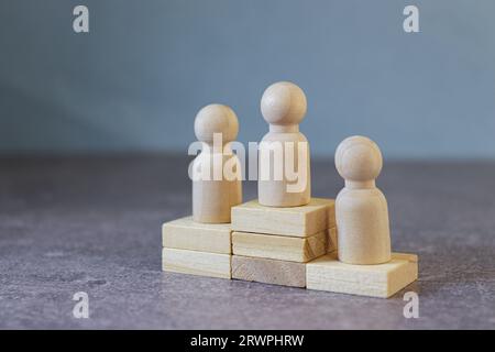 figure di uomini in legno si trovano su un piedistallo dei loro cubetti su uno sfondo blu. Il concetto di rivalità nello sport, nel business e nella vita. Raggiungere il successo Foto Stock