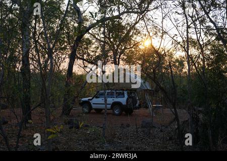 Un'auto con una tenda sul tetto in un campeggio nel Bush, vista attraverso gli alberi al tramonto nel Litchfield National Park, Northern Territory, Australia Foto Stock