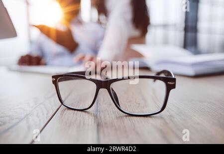 Gli occhiali sono sul tavolo da lavoro. Su uno sfondo sfocato, il ragazzo lavora con un notebook e prende appunti in un notebook. Foto Stock