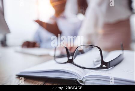 Gli occhiali sono sul tavolo da lavoro. Su uno sfondo sfocato, il ragazzo lavora con un notebook e prende appunti in un notebook. Foto Stock