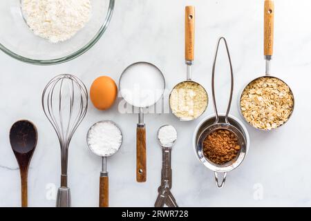 Diversi utensili da forno con ingredienti in fila su un tavolo in marmo bianco. Foto Stock