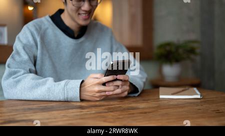 L'immagine ritagliata di un giovane asiatico felice ama chattare con gli amici o utilizzare una nuova applicazione mobile sullo smartphone mentre si rilassa in un cocco Foto Stock