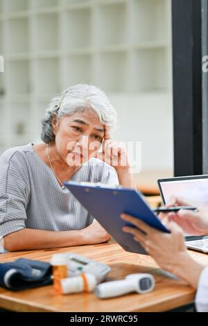 Una vecchia paziente asiatica in pensione stressata e preoccupata viene diagnosticata, ascoltando la sua diagnosi di salute da un medico in una sala esame in un Foto Stock