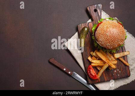 Hamburger fatti in casa con ingredienti di manzo, pomodori, lattuga, formaggio, cipolla, i cetrioli e le patatine fritte sul tagliere e rusty sfondo. Vista superiore Foto Stock