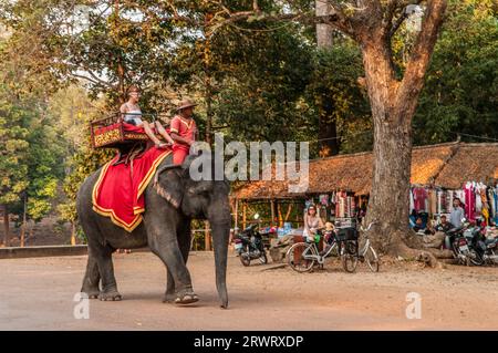 Un mahout e il suo elefante trasportano una turista femminile davanti a un souvenir sul tetto di paglia si trova vicino alla porta sud di Angkor Thom, Cambogia. © Kraig Lieb Foto Stock