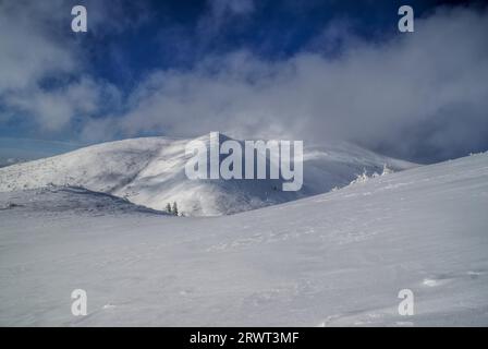 Vista pittoresca di nuvole passando su pendii innevati Foto Stock