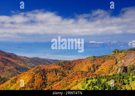 Una vista lontana della foresta di foglie autunnali, della città di Nagano e delle Alpi settentrionali vista dalla vicina Yokotezan-nozoki Foto Stock