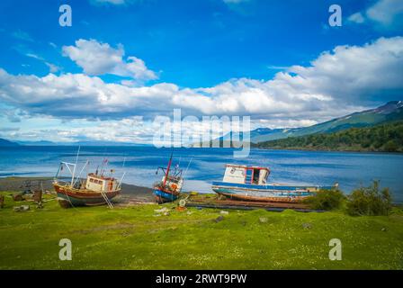 Foto di barche in legno sulla costa del mare con vegetazione vicino alla catena montuosa Dientes de Navarino in Cile Foto Stock