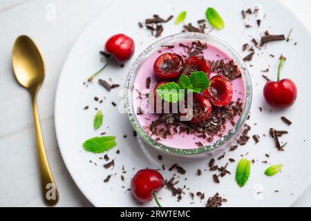 Panna cotta alla ciliegia servita in un bicchiere con frutta fresca e cioccolato grattugiato. Foto Stock