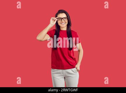 Ritratto di una giovane donna felice con classici occhiali da vista neri isolati su sfondo rosso. Foto Stock