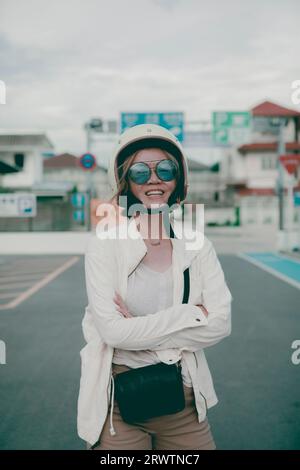 donna che indossa un elmetto di sicurezza in piedi sulla strada cittadina sorride con la felicità del viso Foto Stock