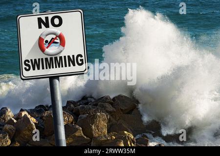 Nessun cartello per nuotare. Grandi onde del mare si infrangono sulle rocce sullo sfondo. Foto Stock