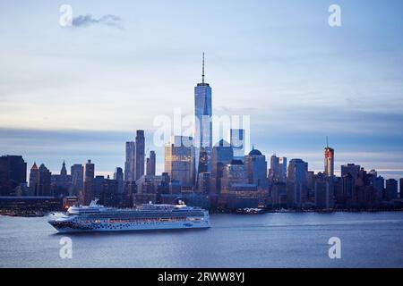 Una barca a vela che naviga di fronte all'iconico skyline di New York City, con il sole che tramonta all'orizzonte Foto Stock