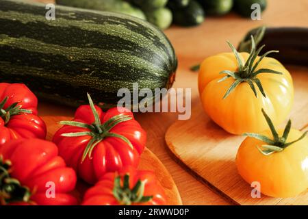 Pomodori grandi maturi, melanzane, verdure su un locale di lavoro in legno della cucina. Molte verdure crude di fondo. Pomodoro, cetrioli. Fornello a casa che fa una h Foto Stock