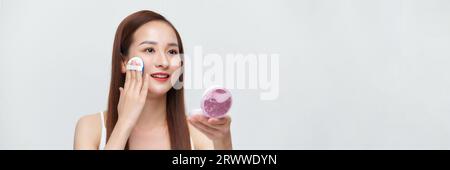 Striscione di una donna cosmetica impeccabile e perfetta che mette la polvere sul suo viso in uno sfondo isolato. Foto Stock