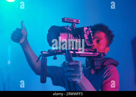 Cameraman professionista che mostra il pollice in alto mentre registra contenuti professionali in studio Foto Stock