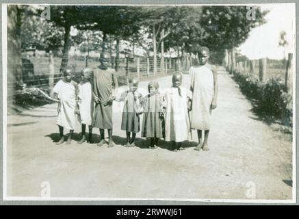 Una delle sette foto intitolate "Kabete Snaps". 1924.» Questa foto mostra un gruppo di quattro donne africane non identificate in piedi con otto bambini e bambini piccoli, per lo più africane ad eccezione di un europeo. Foto Stock
